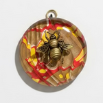 A round glass pendant featuring a metallic gold bee motif over a marbled background of brown, red, and yellow, with a gold hanging loop at the top.