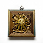 An antique brass wall plaque featuring a relief sun design with a smiling face and surrounding decorative scrollwork, set against a plain white background.