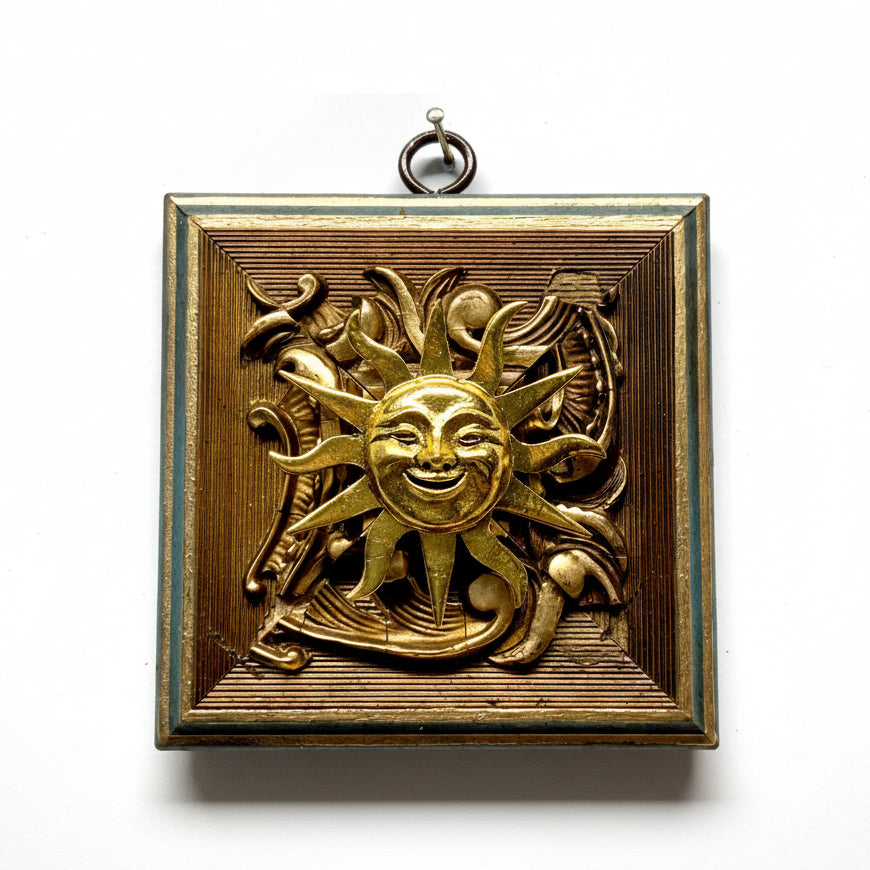 An antique brass wall plaque featuring a relief sun design with a smiling face and surrounding decorative scrollwork, set against a plain white background.