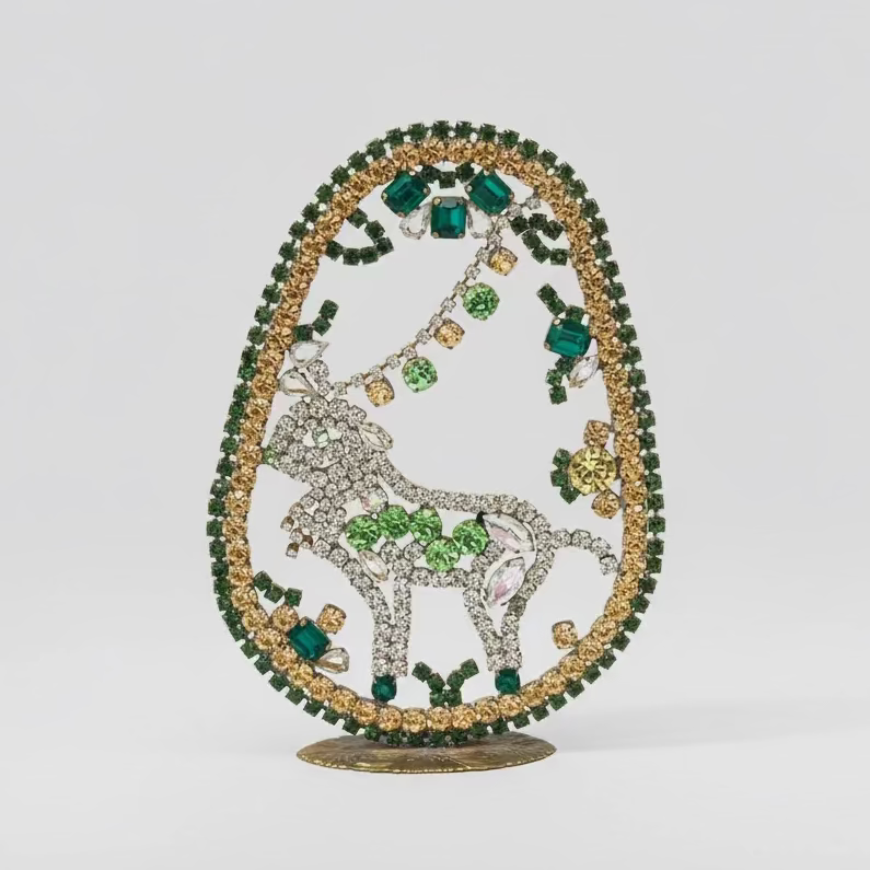 Decorative brooch with green and gold gemstones on a neutral background