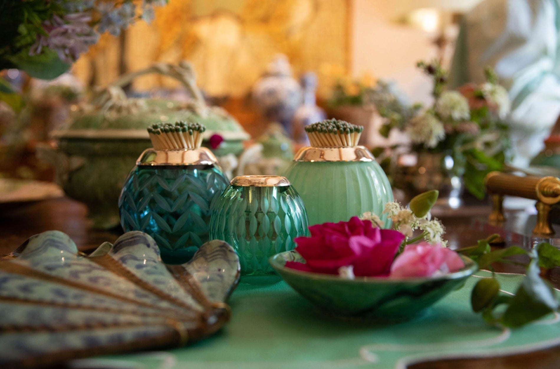 Decorative table setting with teal and gold candle holders and a bowl of pink flowers.