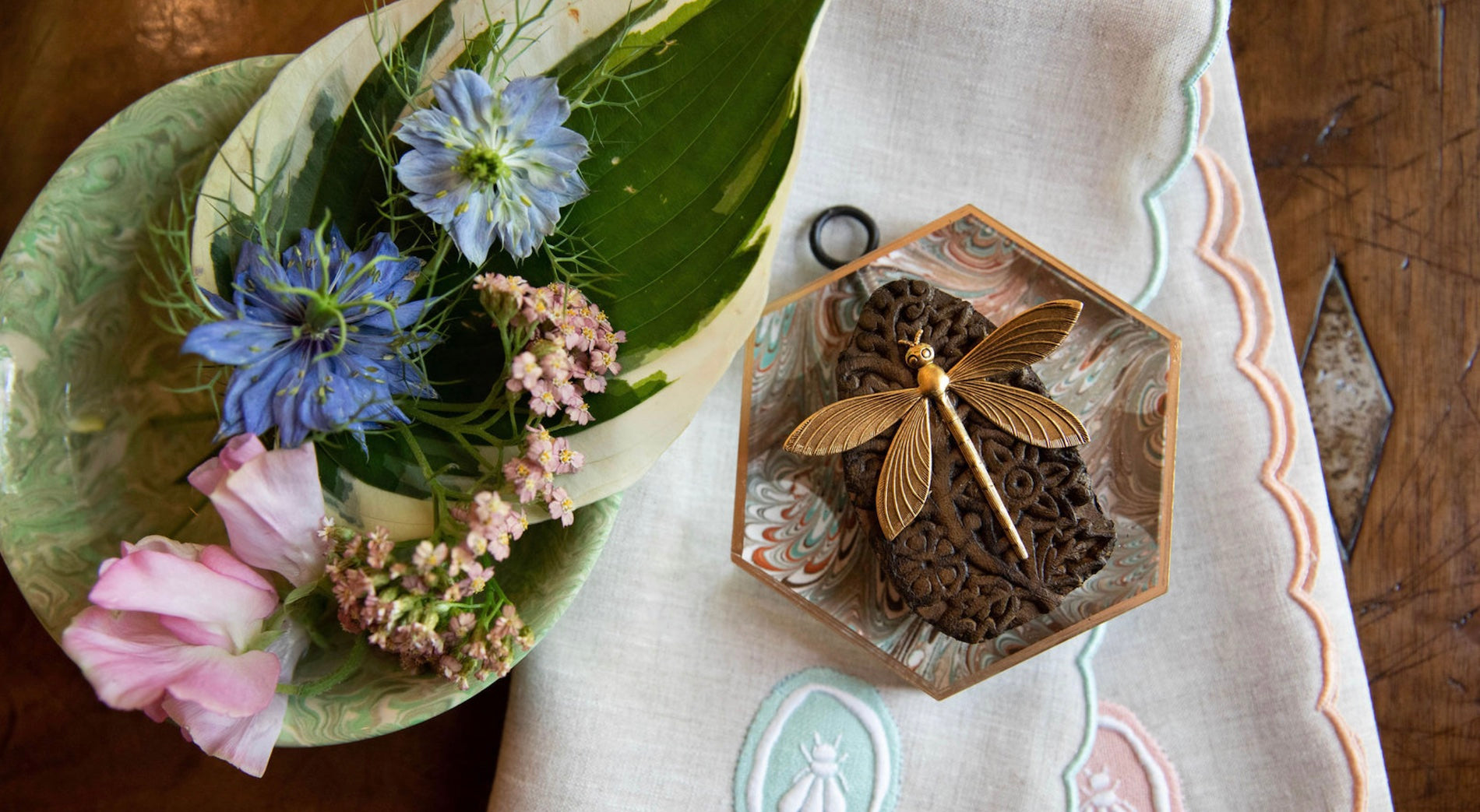Decorative plate with flowers and a dragonfly-shaped object on a patterned tablecloth.