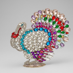 Decorative brooch shaped like a turkey with multicolored gemstones on a beige background