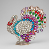Decorative brooch shaped like a turkey with multicolored gemstones on a beige background